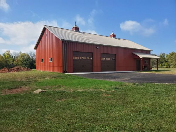 A red barn with two garage doors is sitting in the middle of a grassy field.