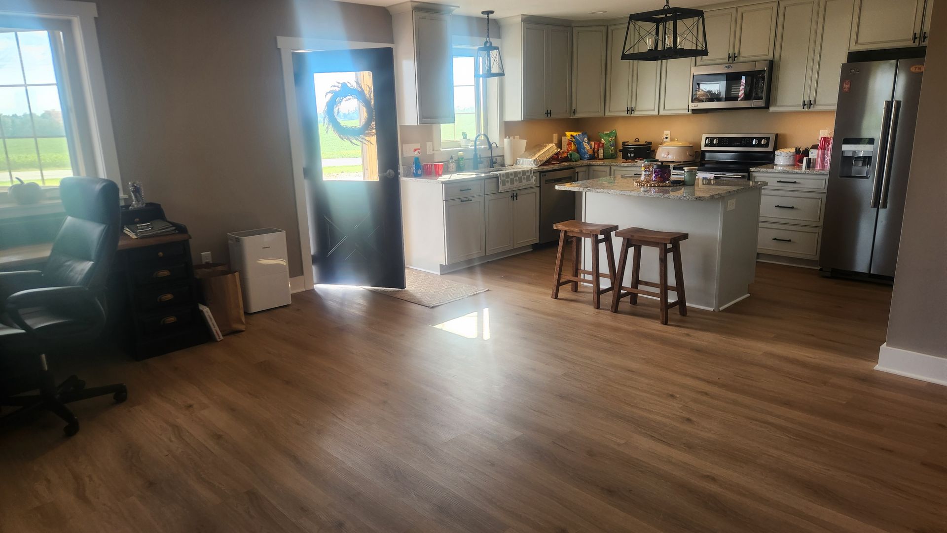 A kitchen with hardwood floors , stools , a refrigerator and a desk.