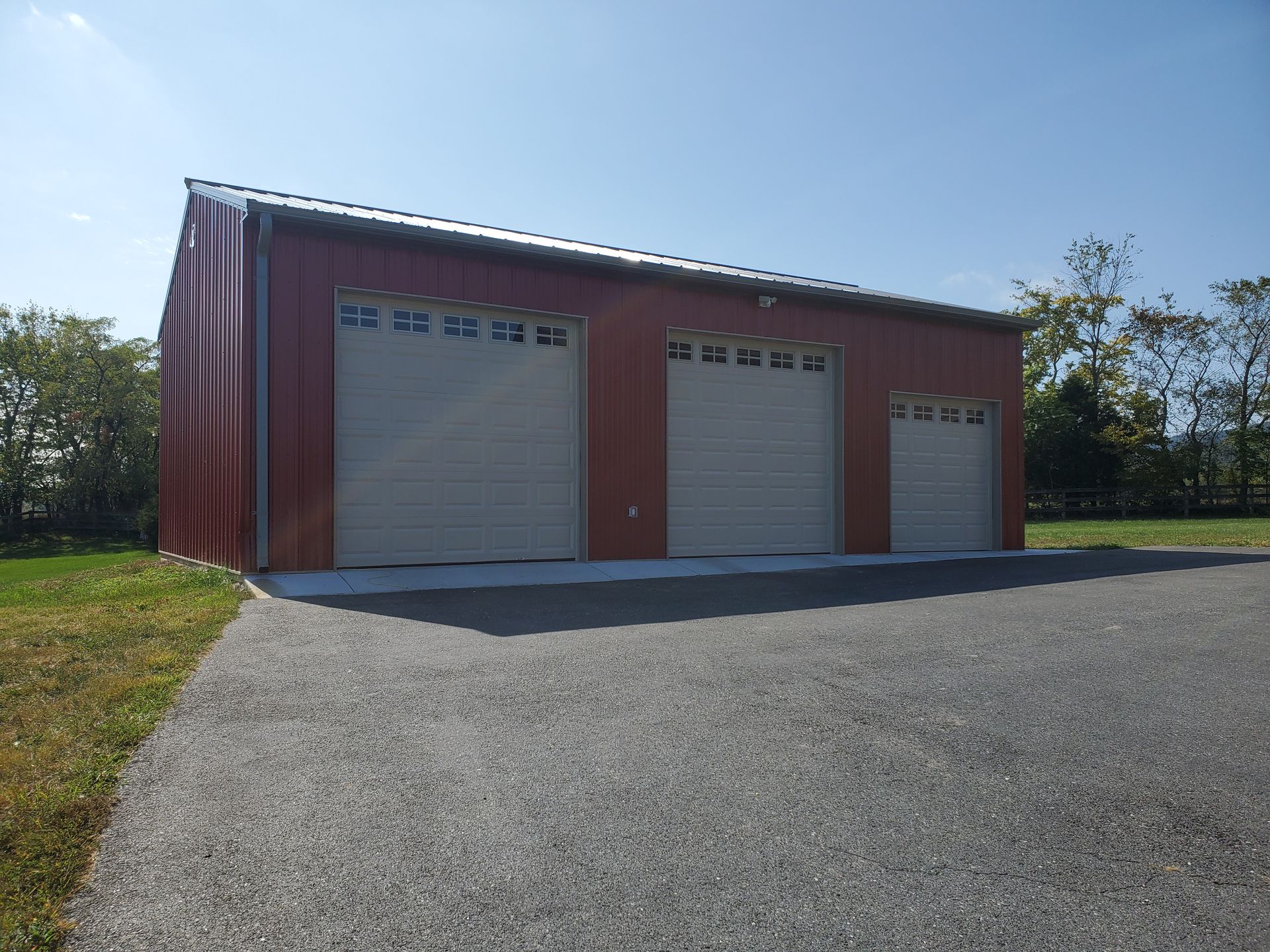 A red garage with three white garage doors is sitting on top of a gravel driveway.