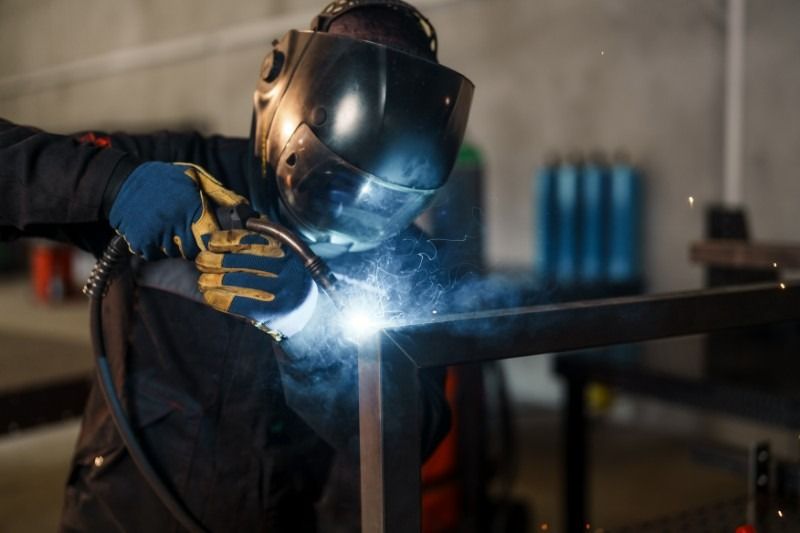 Welder in protective gear welding metal frame, sparks flying, workshop setting.