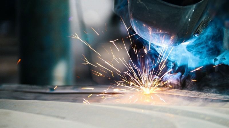 Welder using torch, creating sparks and blue light.