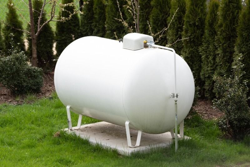 White propane tank in a yard, with green grass and trees in the background.