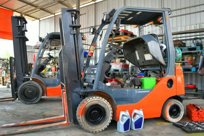 Two orange and gray forklifts in a repair shop. One has its engine cover open.