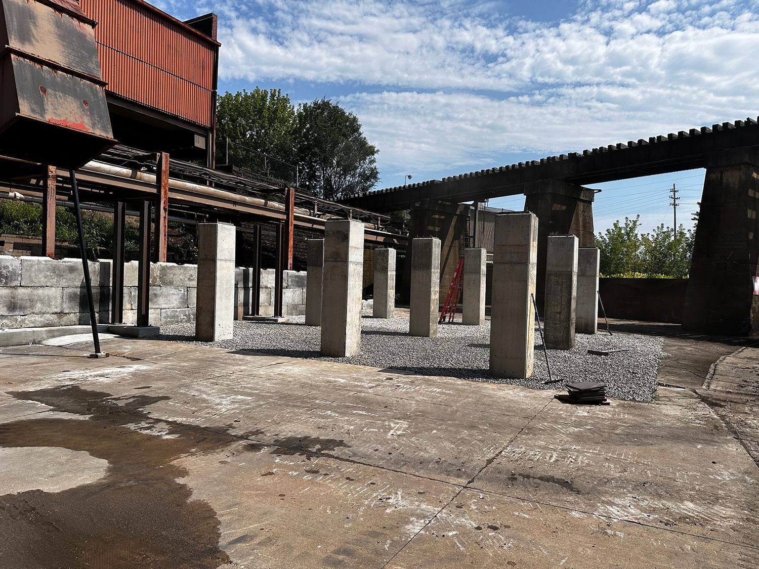 A row of concrete pillars in an empty area with a bridge in the background.