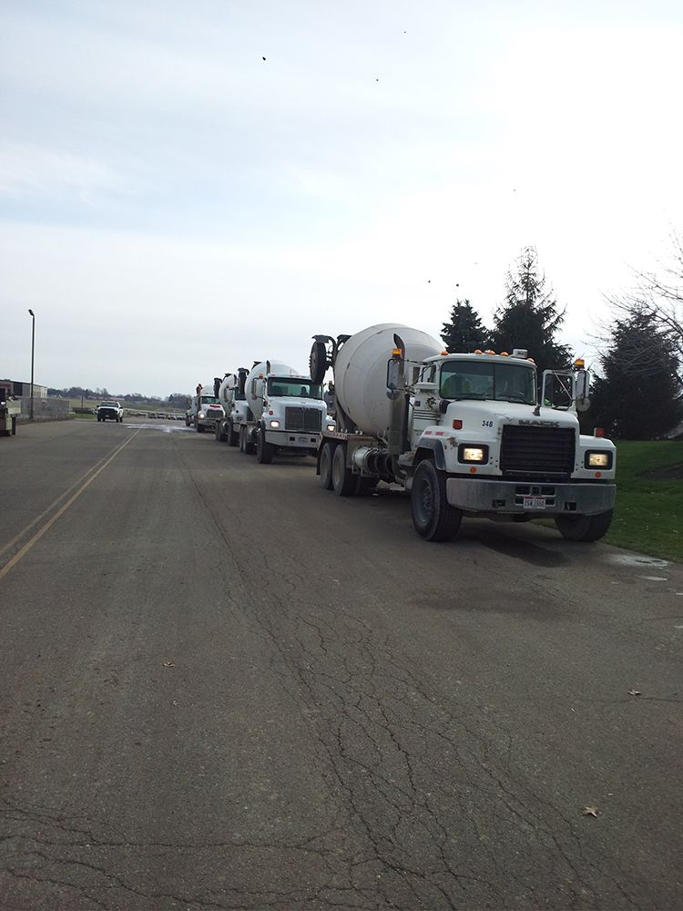 A row of cement trucks are driving down a road