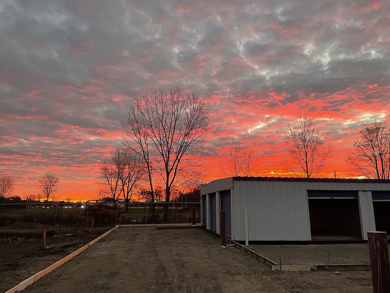 A garage with a sunset in the background and trees in the foreground.