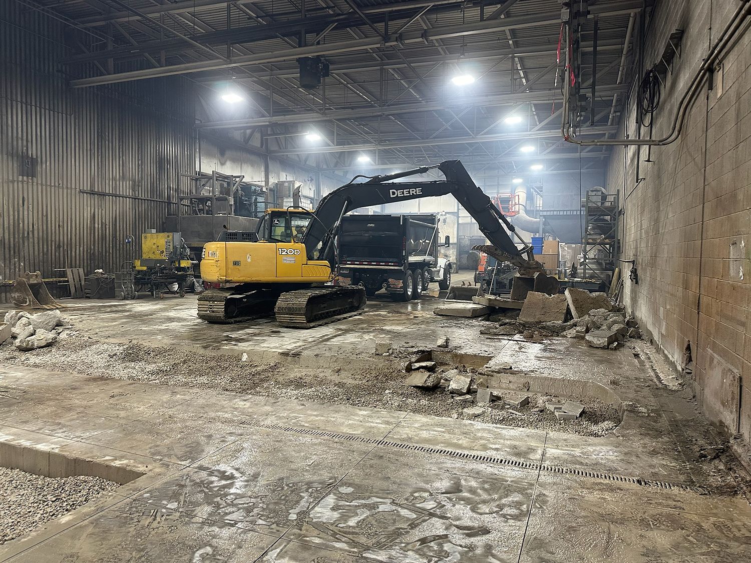 A yellow excavator is working in a large warehouse.