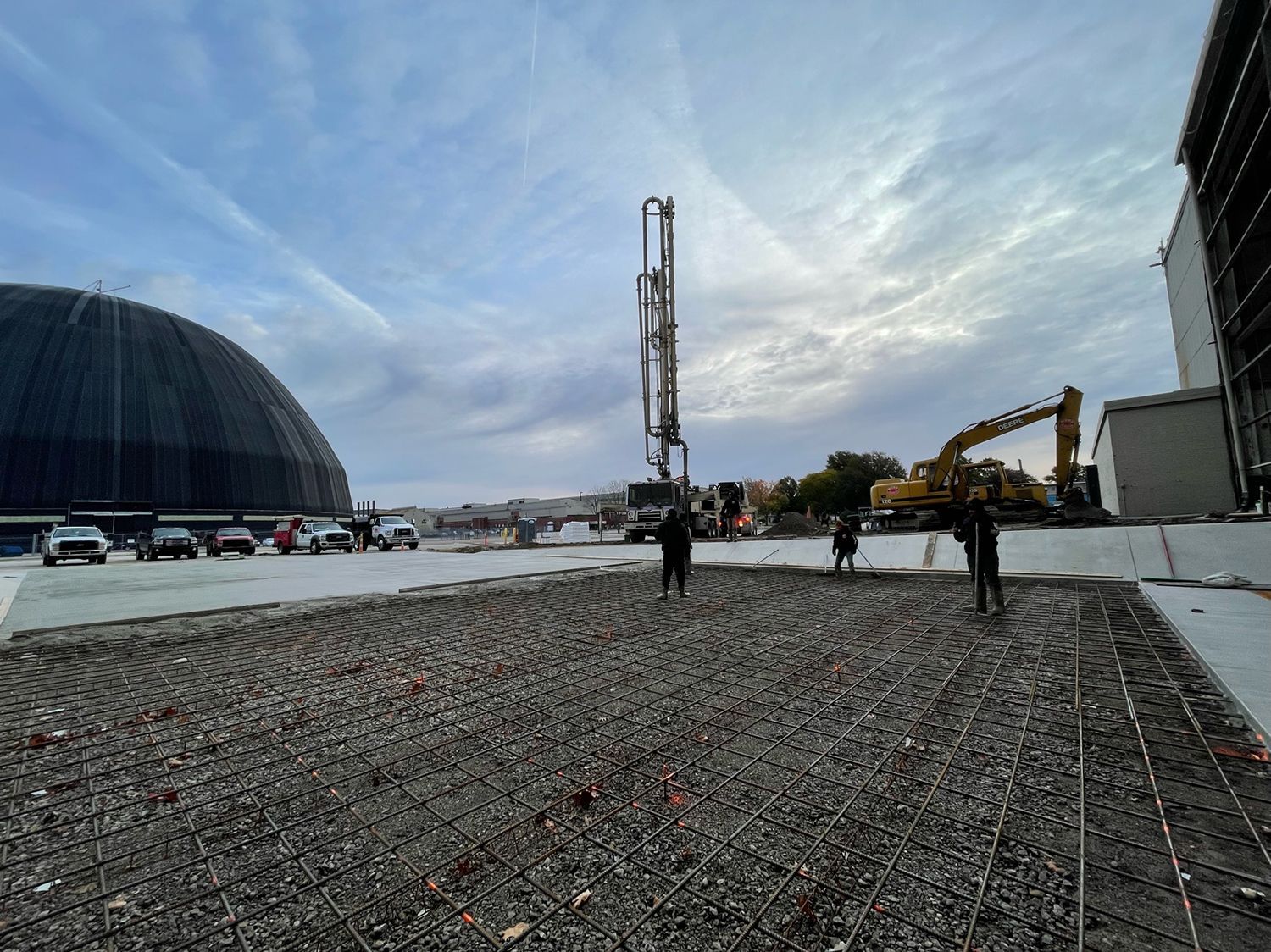 A construction site with a large dome in the background and a concrete pump in the foreground.
