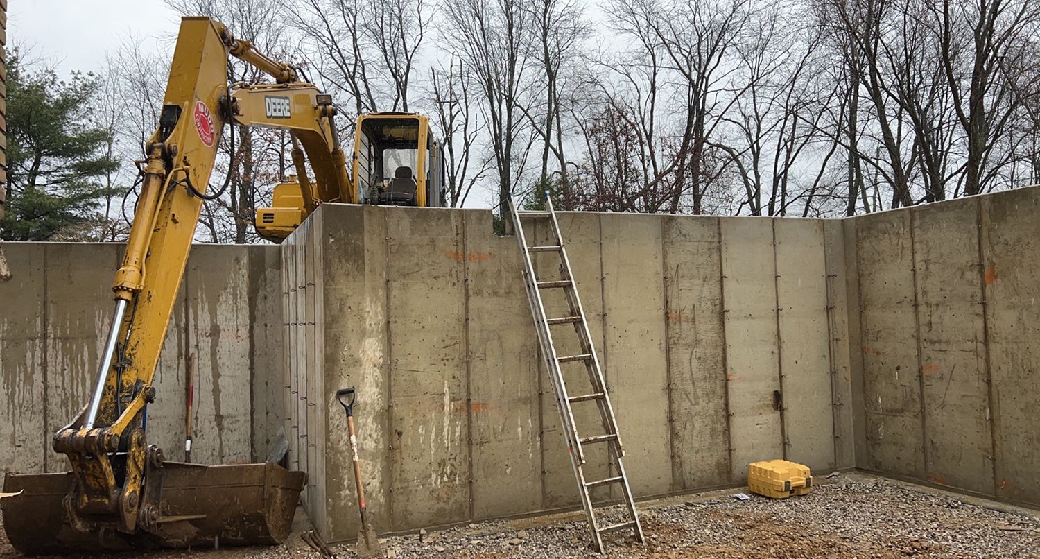 A yellow excavator is sitting on top of a concrete wall next to a ladder.