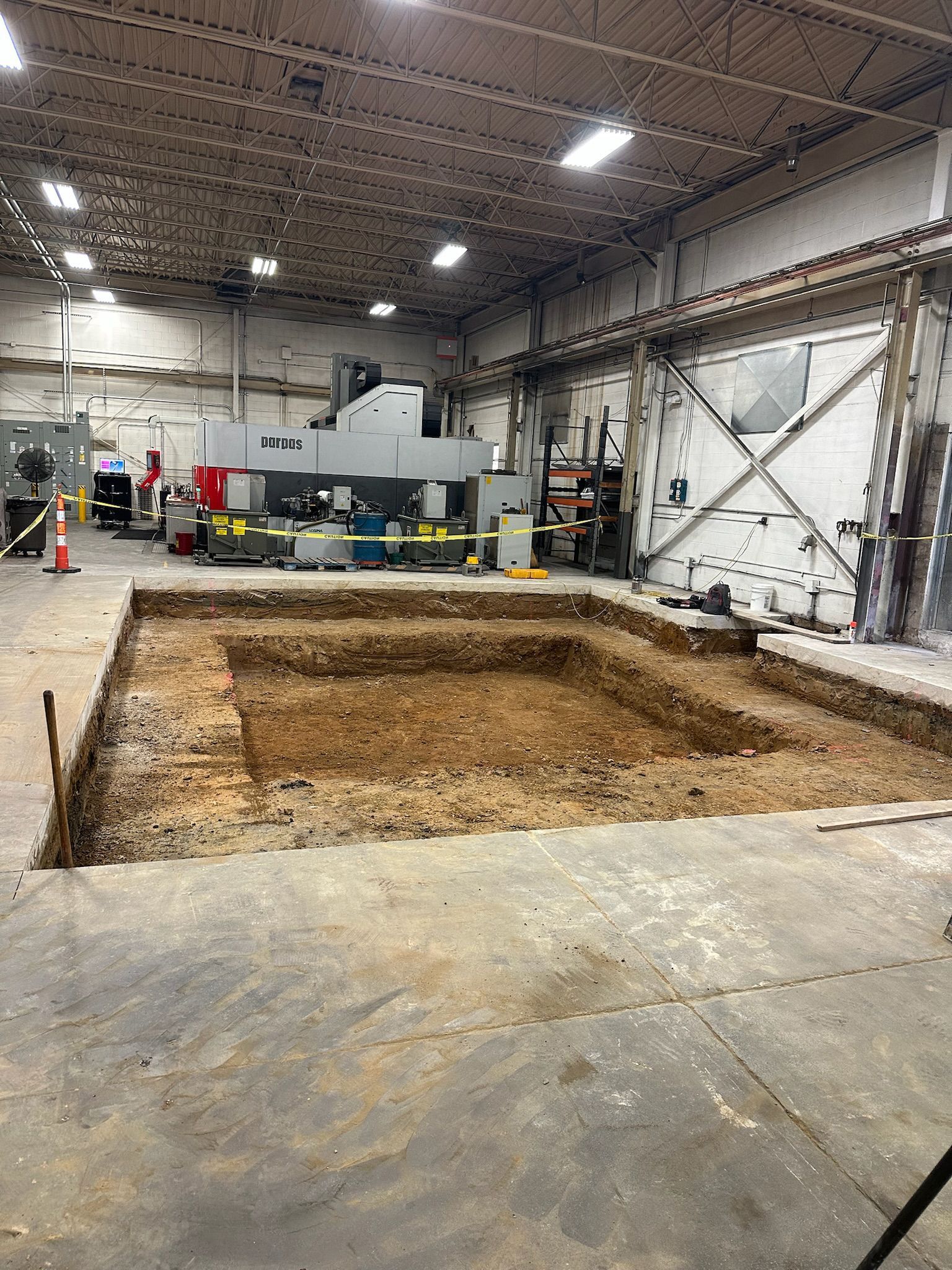 A large hole in the ground in a warehouse with a machine in the background.