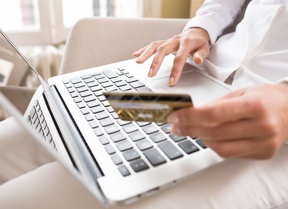A person is holding a credit card in front of a laptop computer.