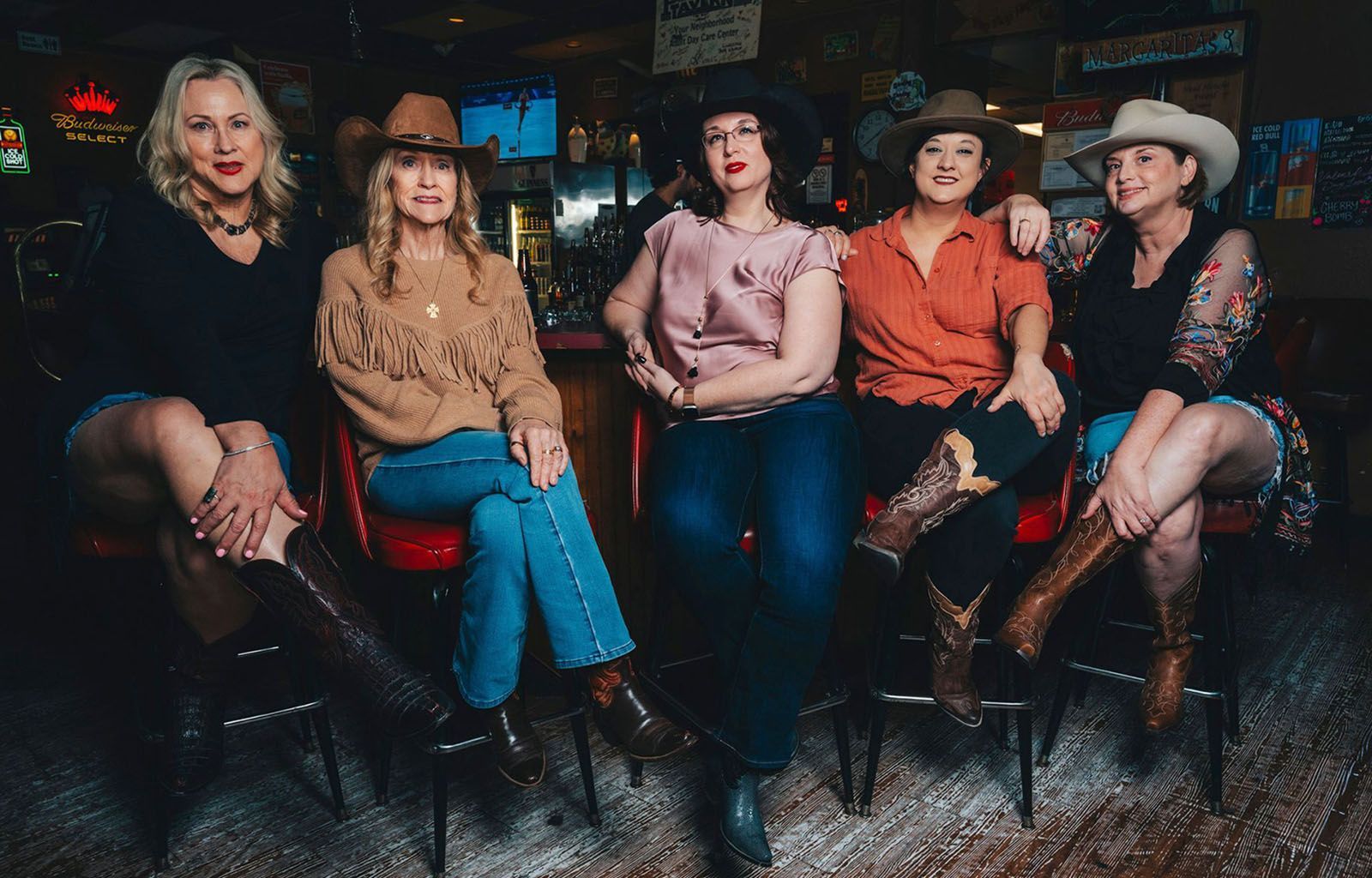 Five women in cowboy hats and boots sitting at a bar