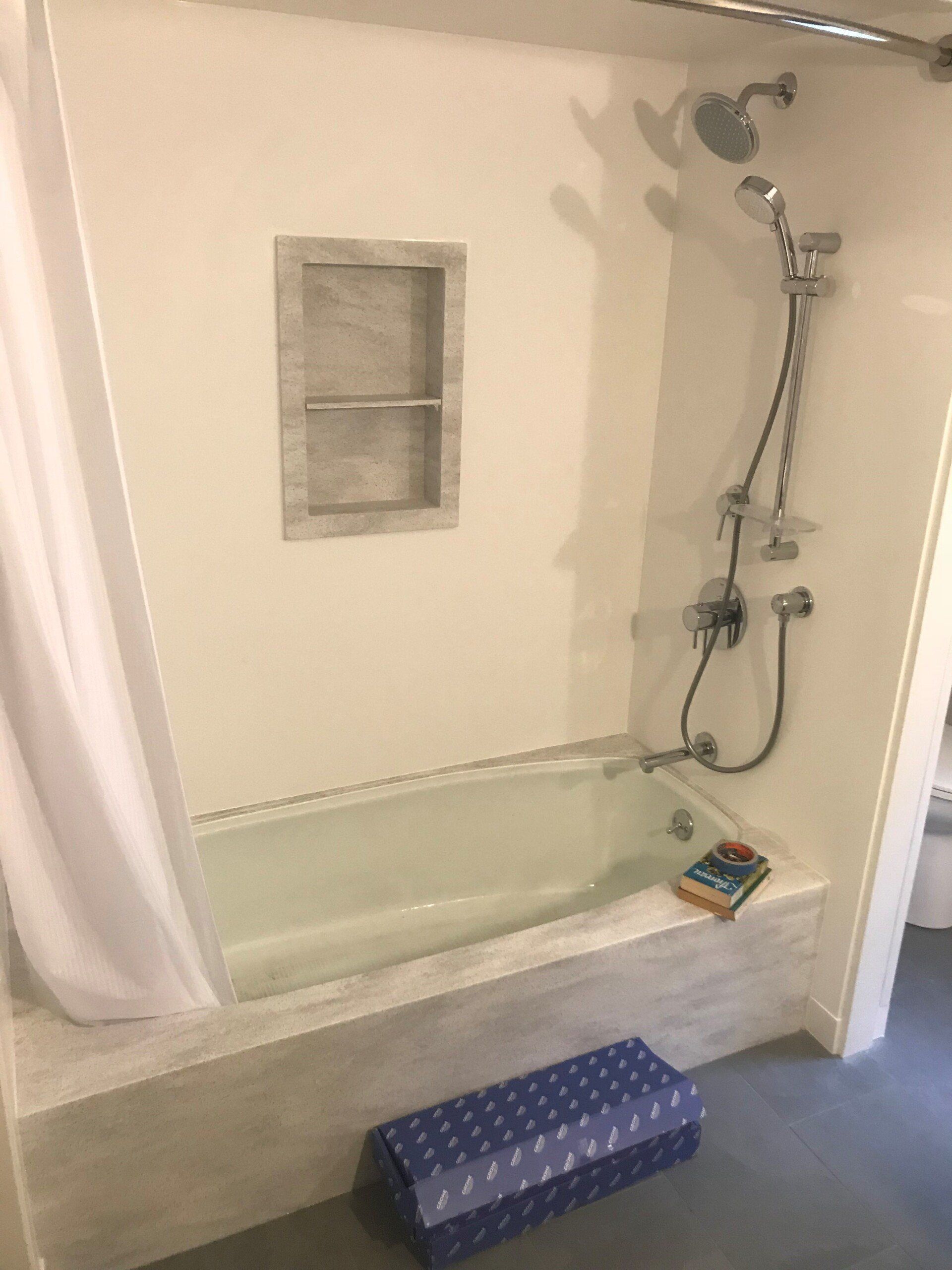 A bathtub in a bathroom with a shower and a book on the floor.