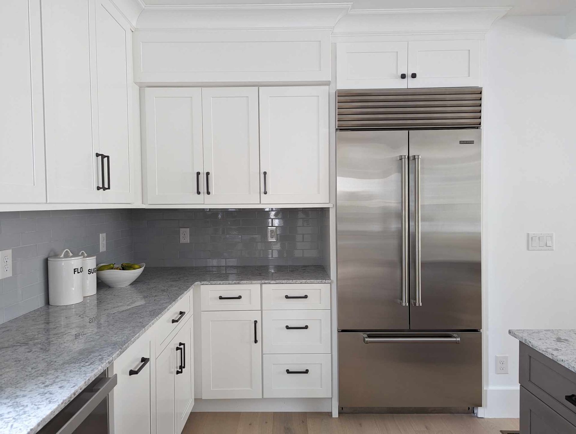 A kitchen with white cabinets and a stainless steel refrigerator.