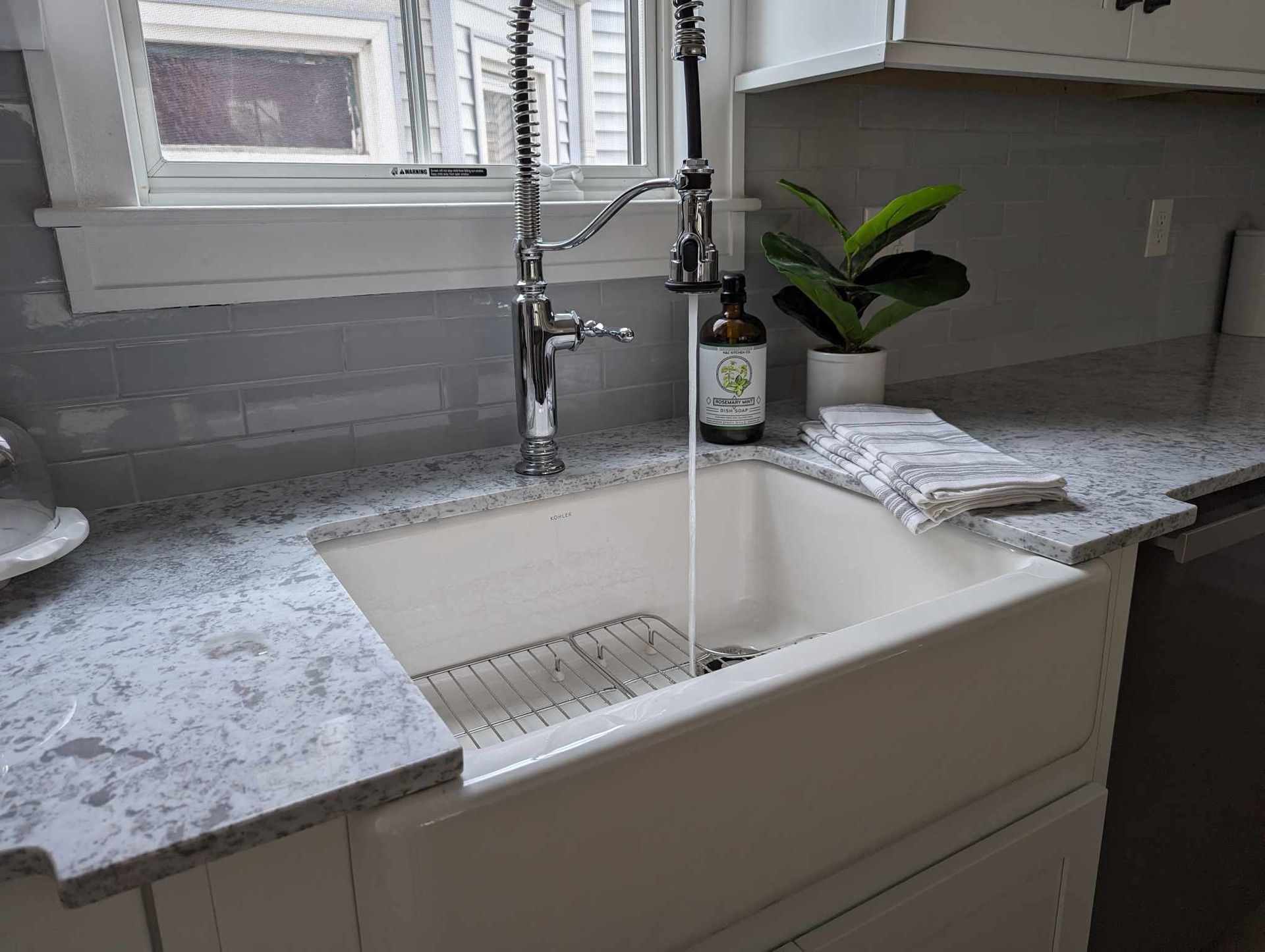 A kitchen sink with water running out of it and a plant on the counter.