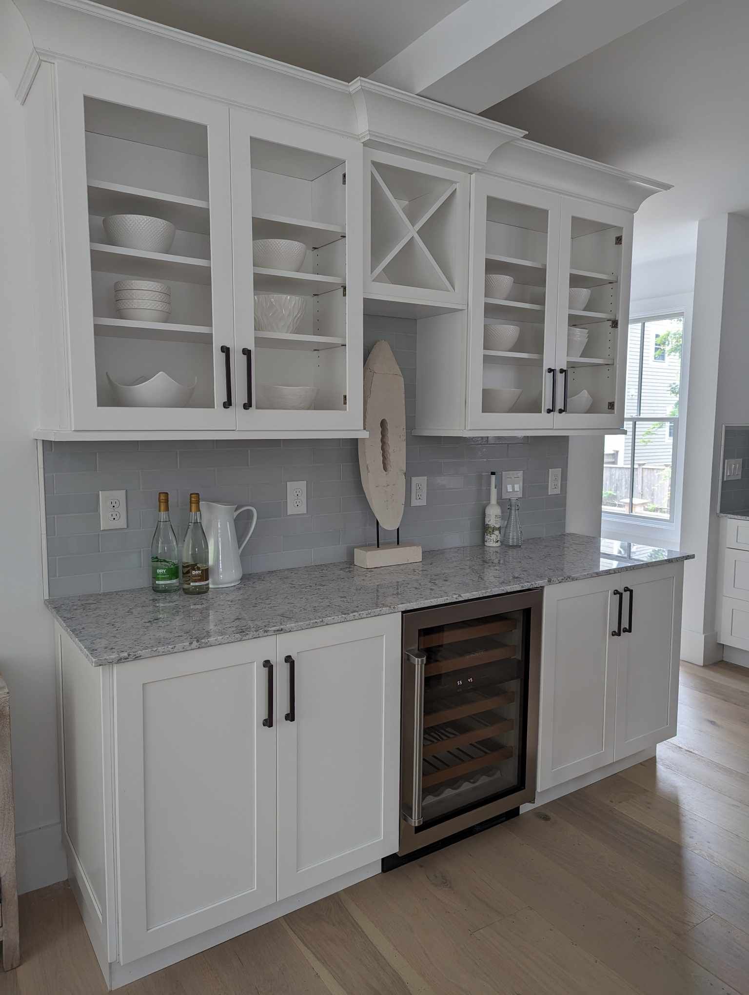 A kitchen with white cabinets, granite counter tops, and a wine cooler.