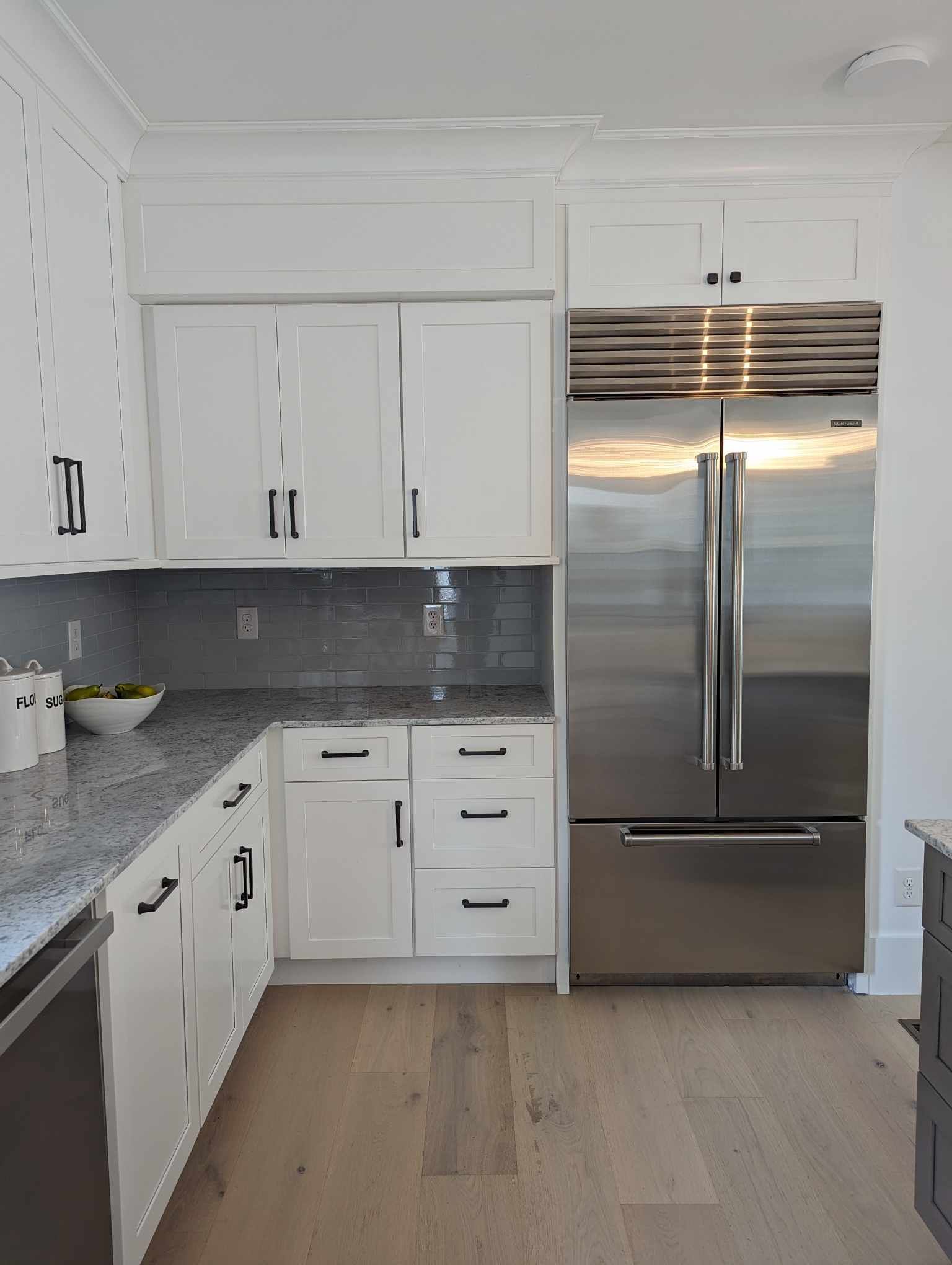 A kitchen with white cabinets and a stainless steel refrigerator.