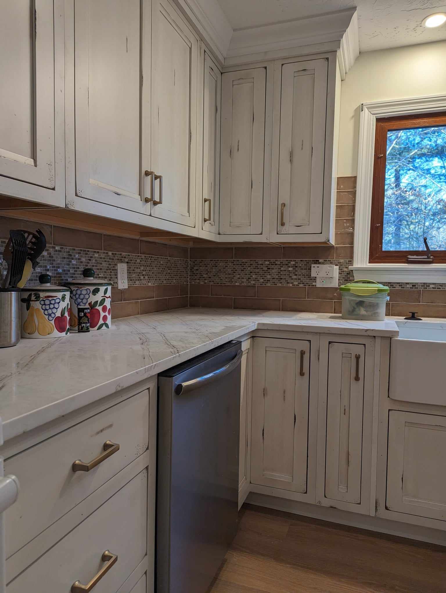A kitchen with white cabinets, a stainless steel dishwasher, a sink, and a window.
