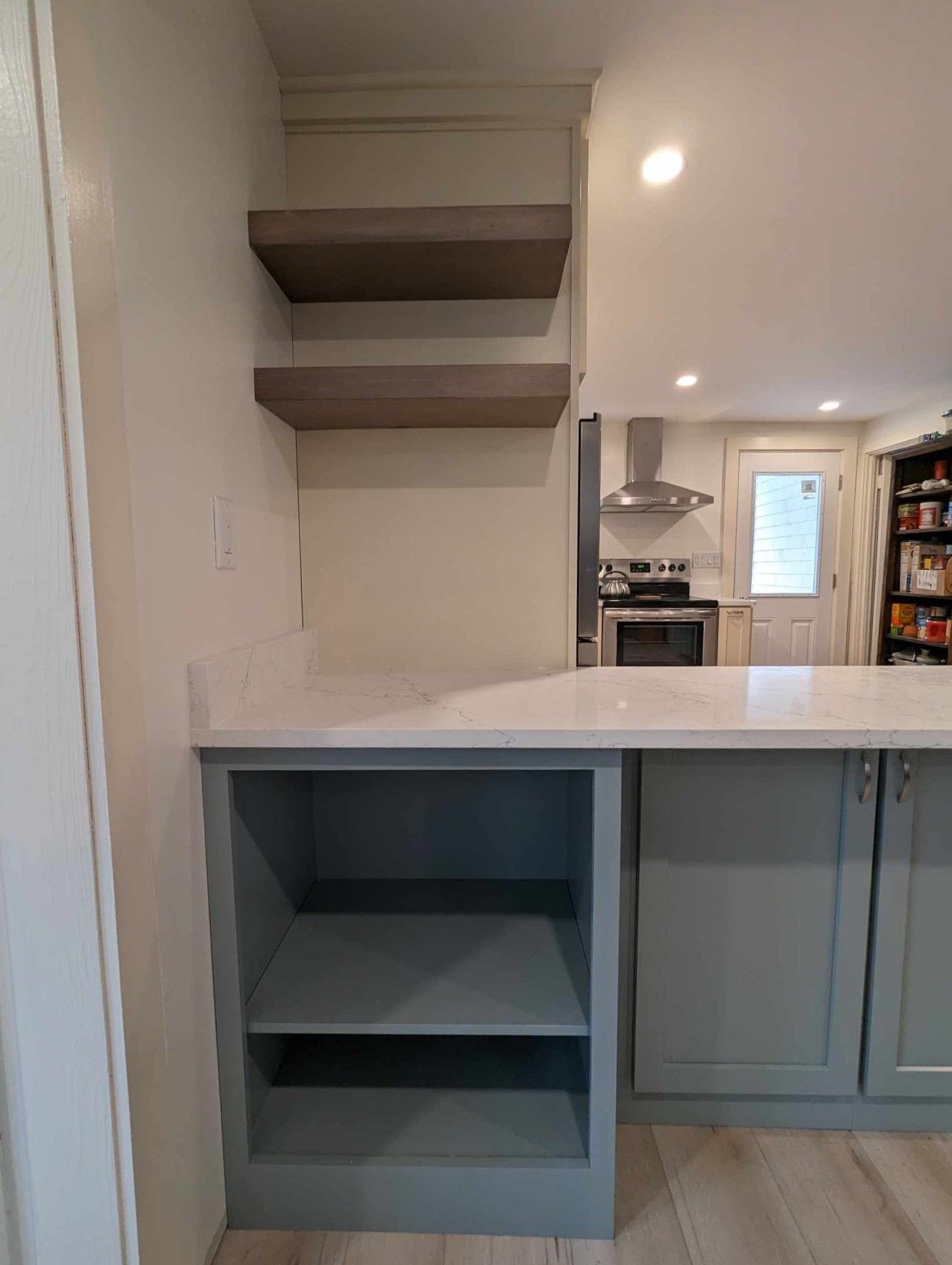A kitchen with a stove, sink, and shelves.