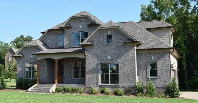 Large gray brick suburban house with a covered porch and a manicured lawn on a sunny day