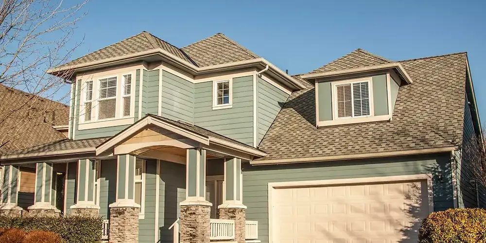 Two-story suburban house with light blue siding, tan roof, and attached garage under a clear sky