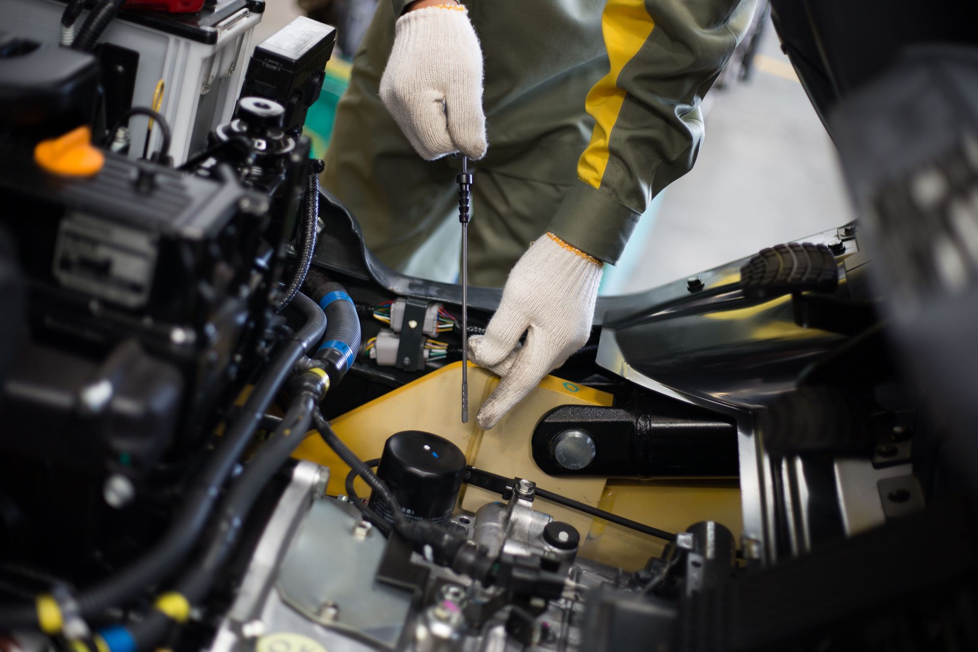 A worker in gloves checks the oil level using a dipstick on an open engine in a workshop setting.