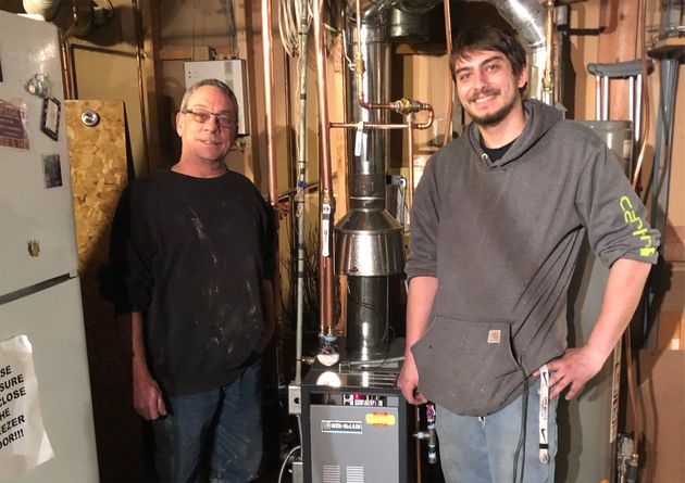 Two people stand smiling next to a newly installed boiler system with copper piping in a basement utility room.