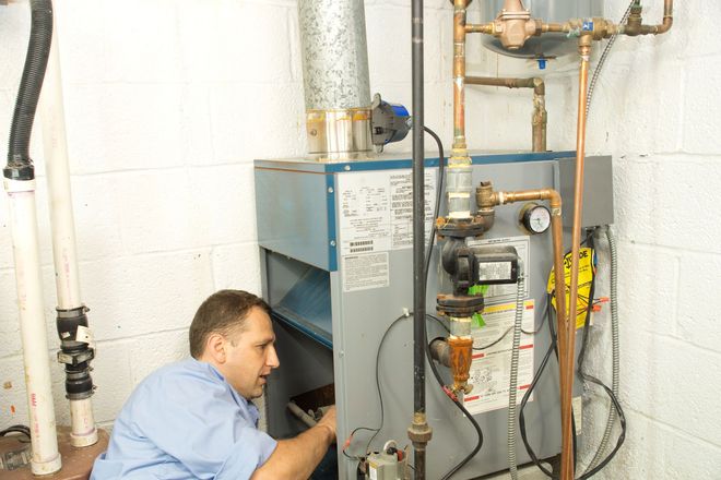 A professional technician inspects the interior of a residential boiler system in a basement.