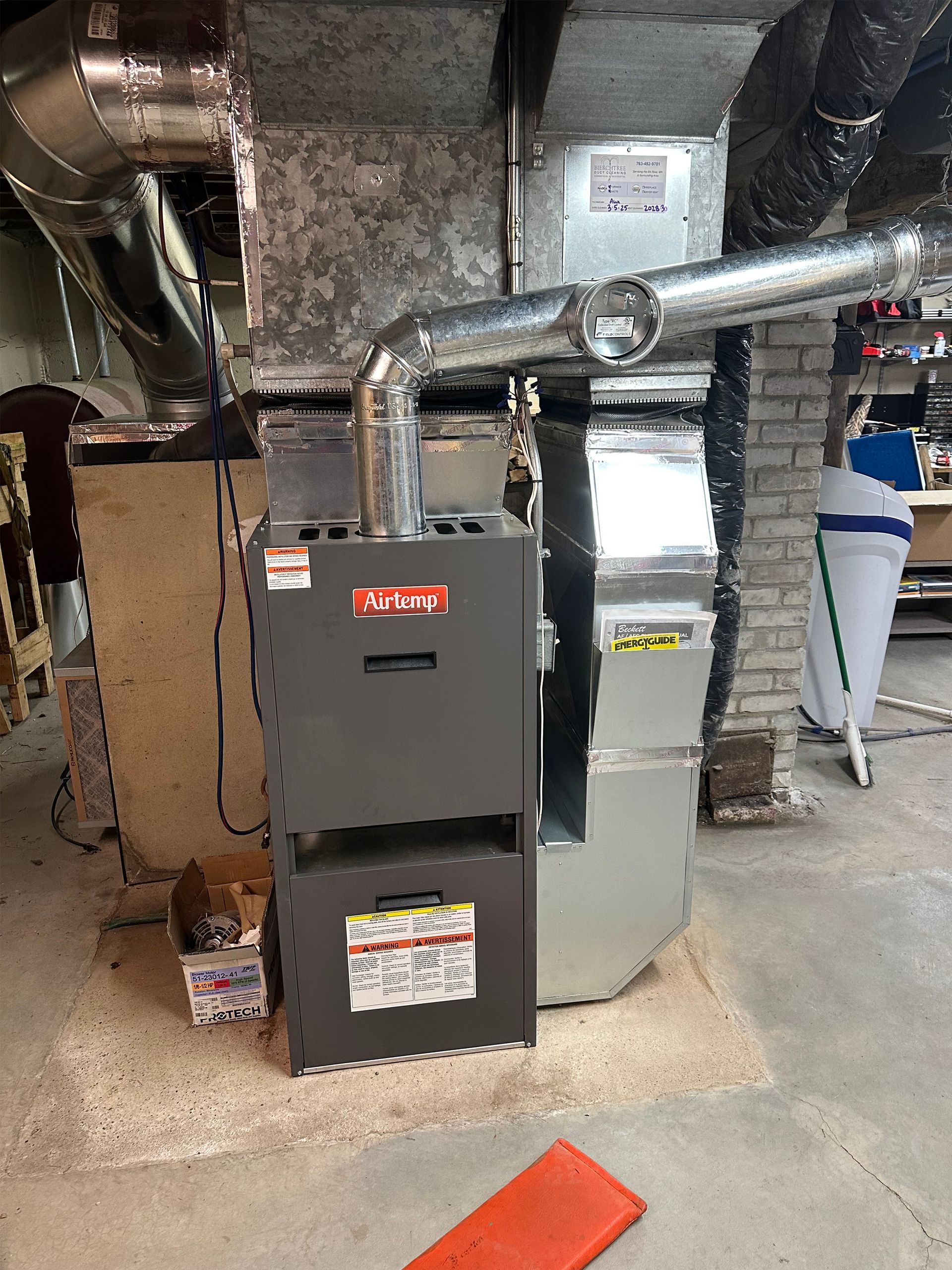 A gray central heating furnace standing on a concrete basement floor, connected to metallic ductwork.
