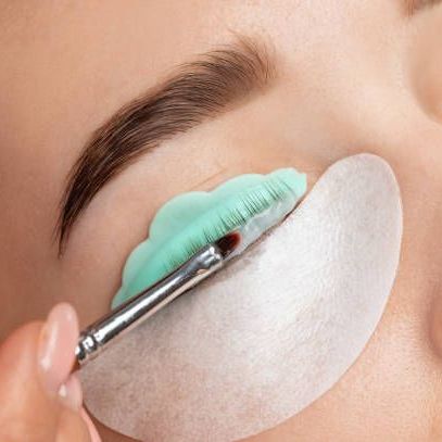 A woman is getting her eyelashes lifted with a brush.