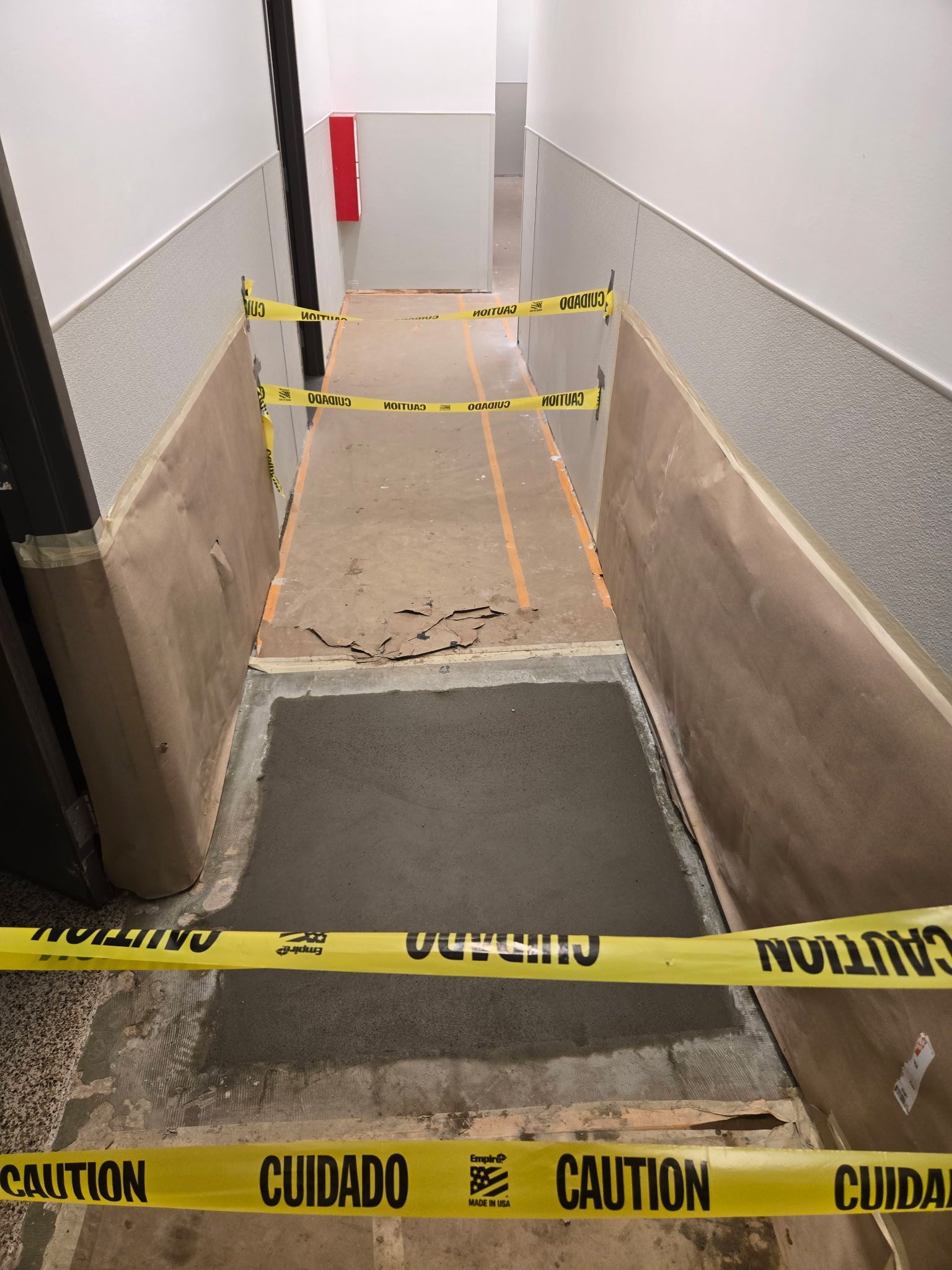 A hallway under construction with a wet cement floor patch, blocked off by yellow caution tape.
