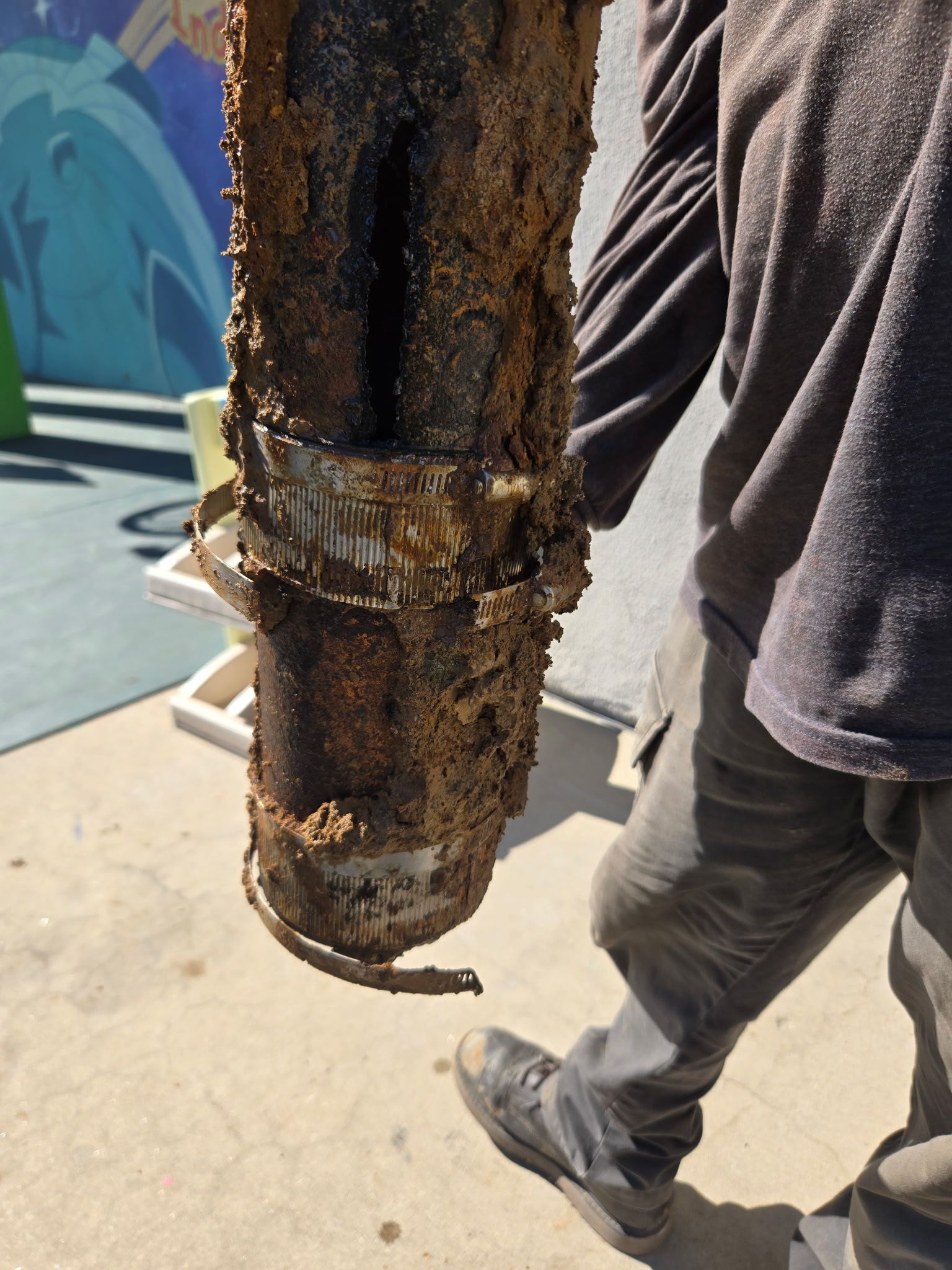 A person holds a piece of heavily corroded and debris-covered pipe segment outdoors.