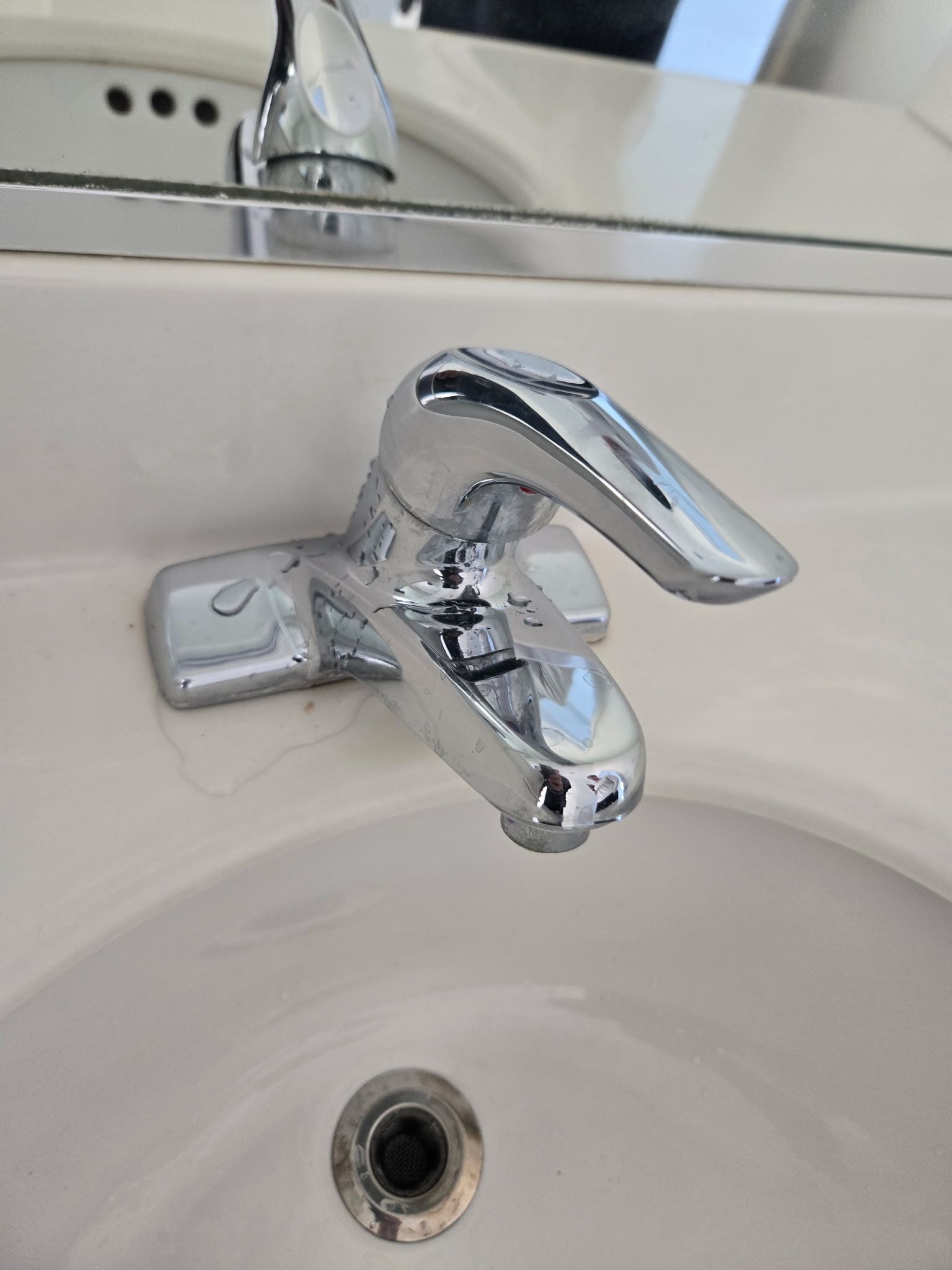A chrome single-handle bathroom faucet mounted on a white porcelain sink vanity.