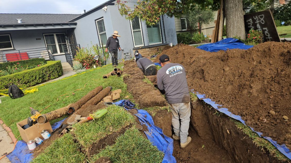 Construction workers excavate a trench in front of a house, using blue tarps to manage dirt on the lawn.