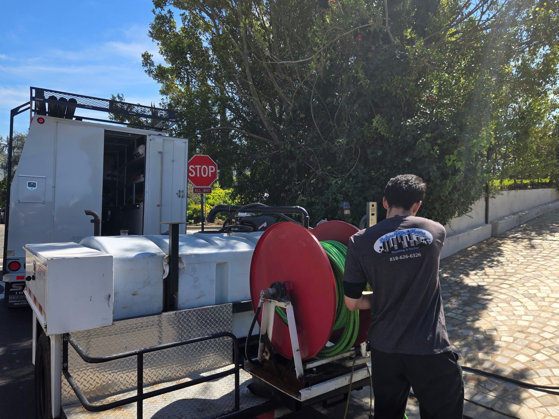 A person in a gray t-shirt operates a hose reel on a mobile equipment trailer parked on a paved driveway.