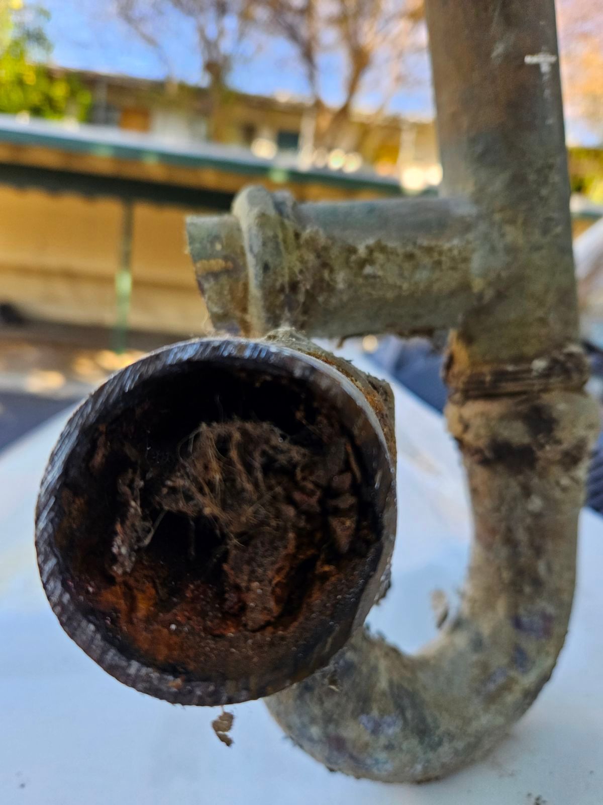 A close-up view of an old, corroded U-shaped metal pipe completely clogged with debris.