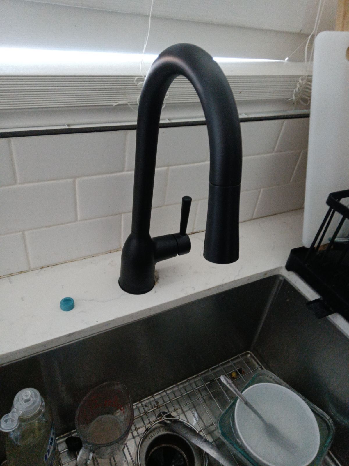 A matte black, high-arch pull-down kitchen faucet sits on a white countertop above a stainless steel sink.
