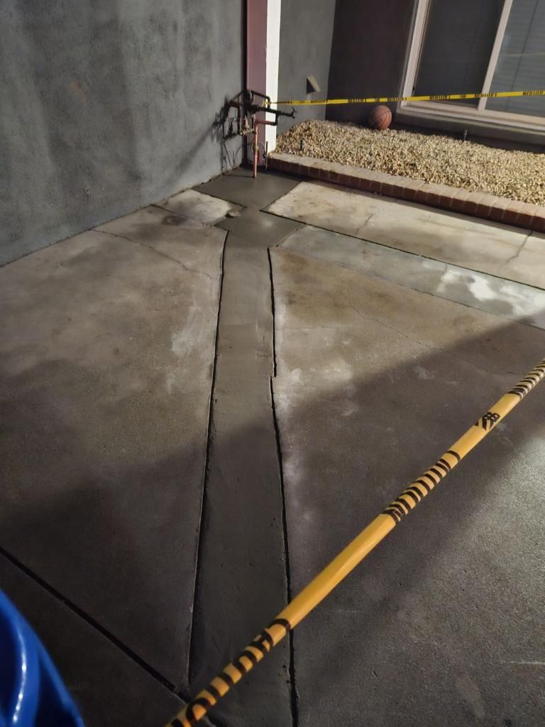 A concrete driveway with a newly poured, darker rectangular patch in the center, cordoned off by yellow caution tape.