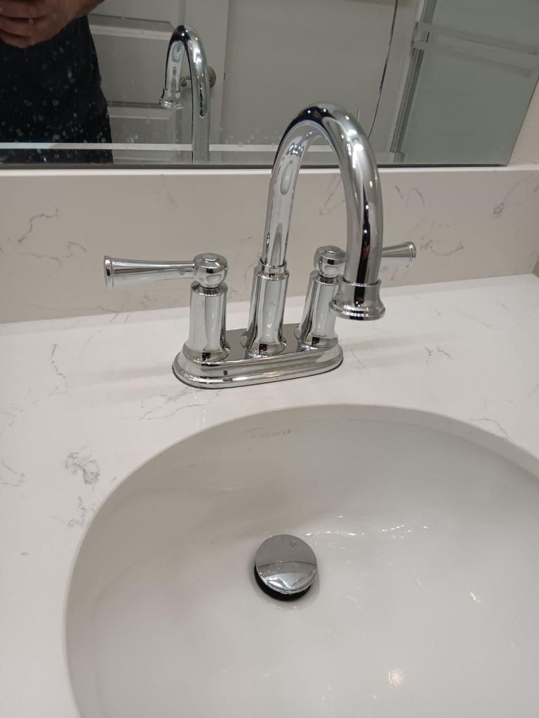 A chrome bathroom faucet with two lever handles mounted on a white, marble-patterned countertop above a white sink.