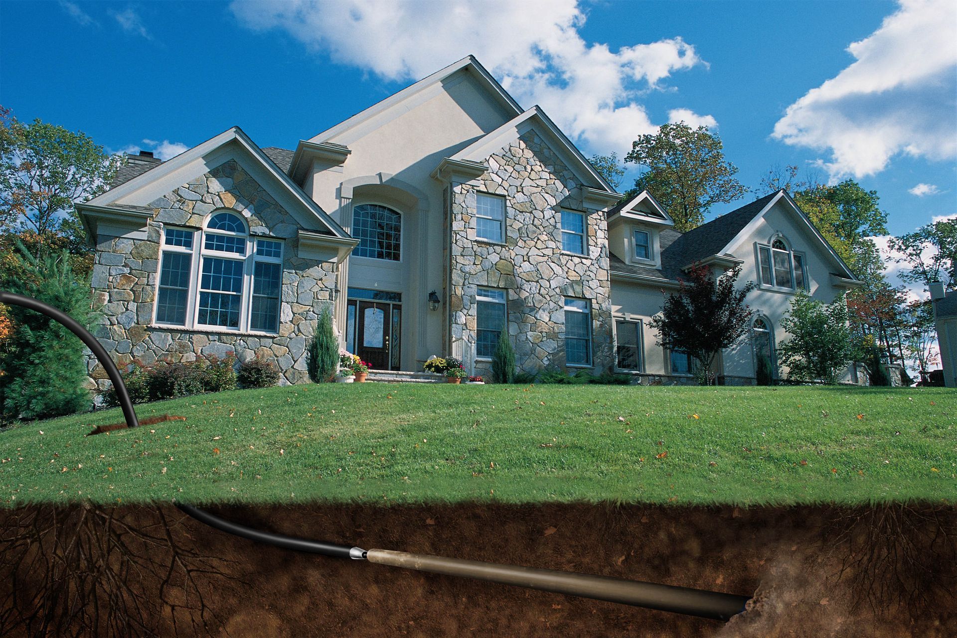 Large stone house with a green lawn; a broken underground pipe is visible in a trench below.