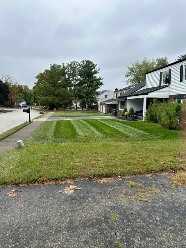 A suburban lawn with freshly mowed stripes in front of a white two-story house under a cloudy sky.