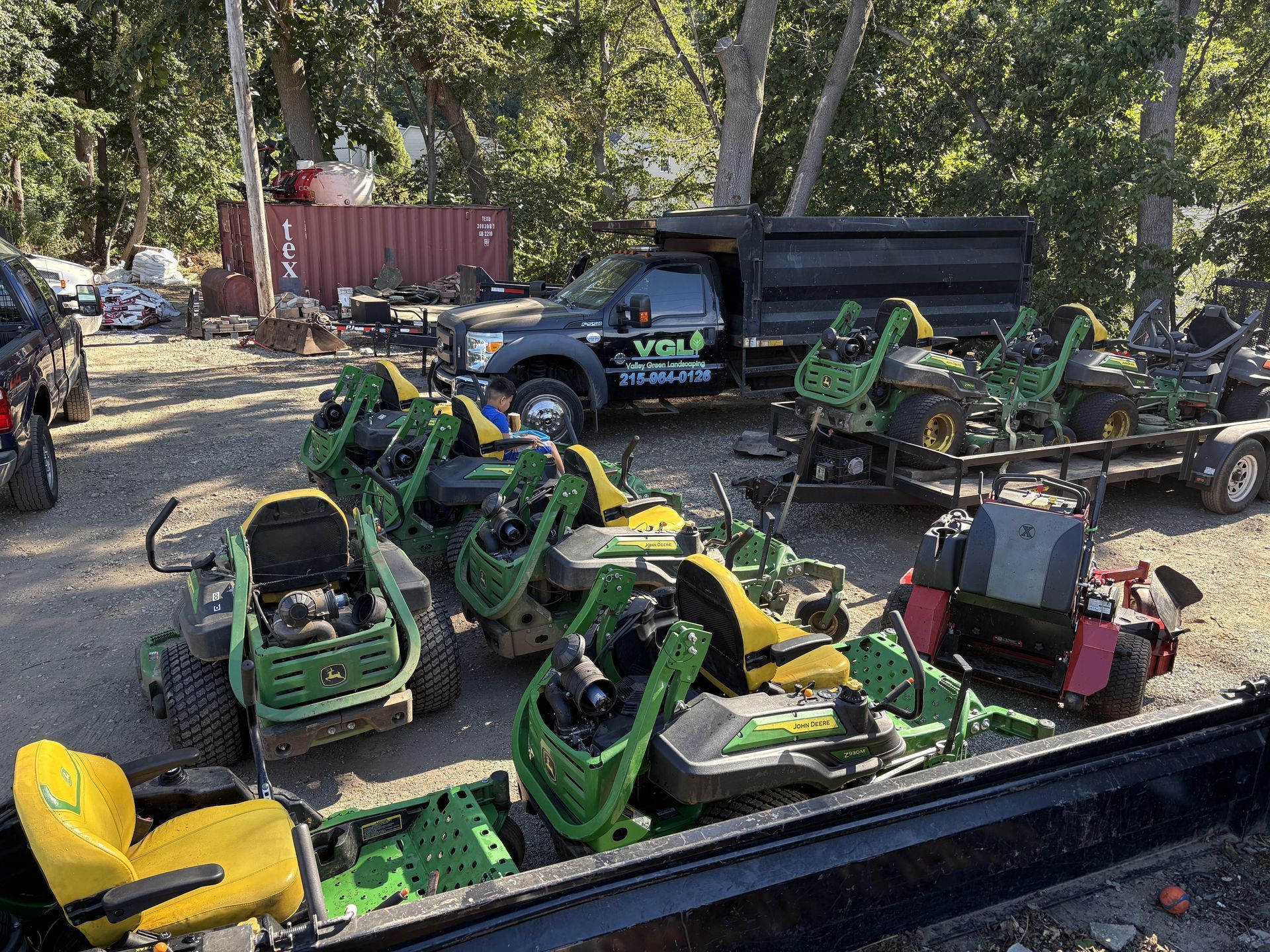 Lawn care equipment: Several riding mowers, plus a truck and trailer, parked outside on a sunny day.