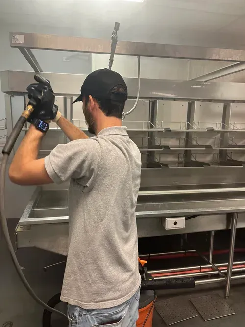 Worker assembling a stainless steel commercial kitchen hood with a power tool in a workshop