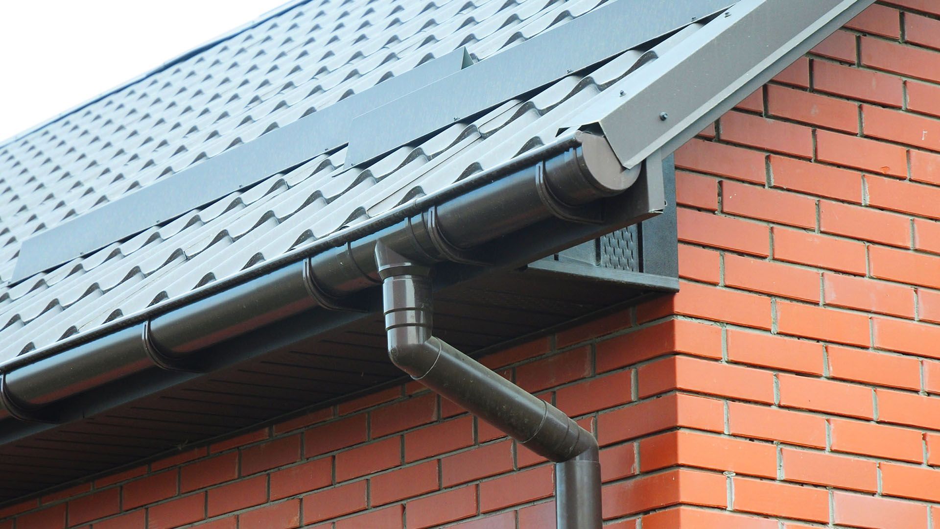 A black gutter is attached to the side of a brick building.