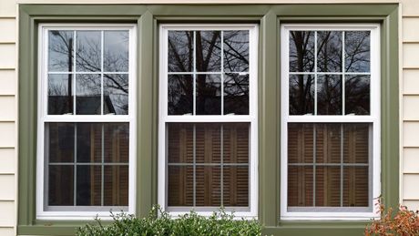 Three windows on a house with green trim and shutters