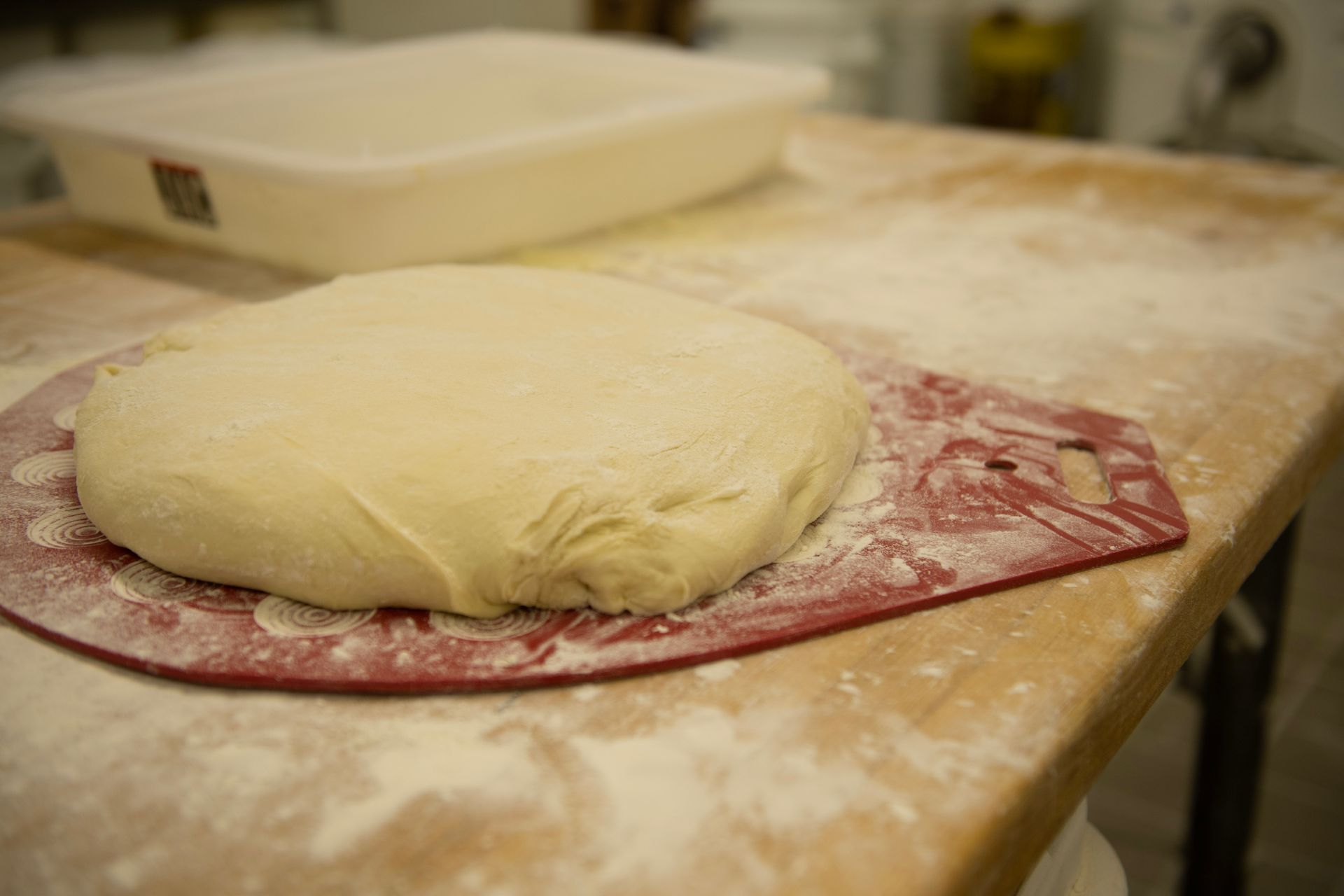 A piece of dough is sitting on a cutting board on a wooden table.