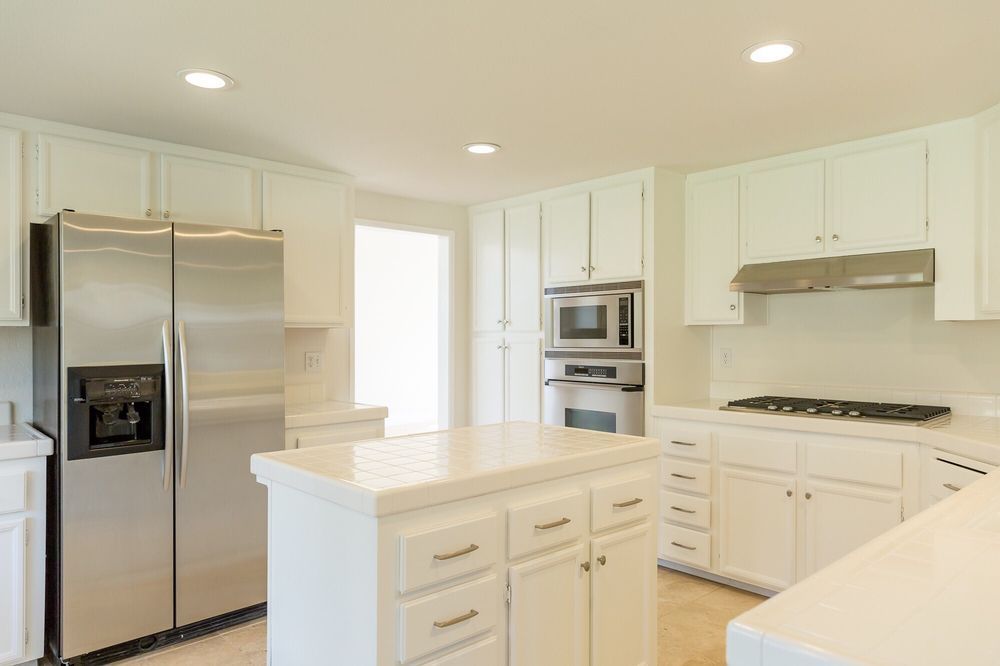 White kitchen with stainless steel refrigerator, cabinets, and island.