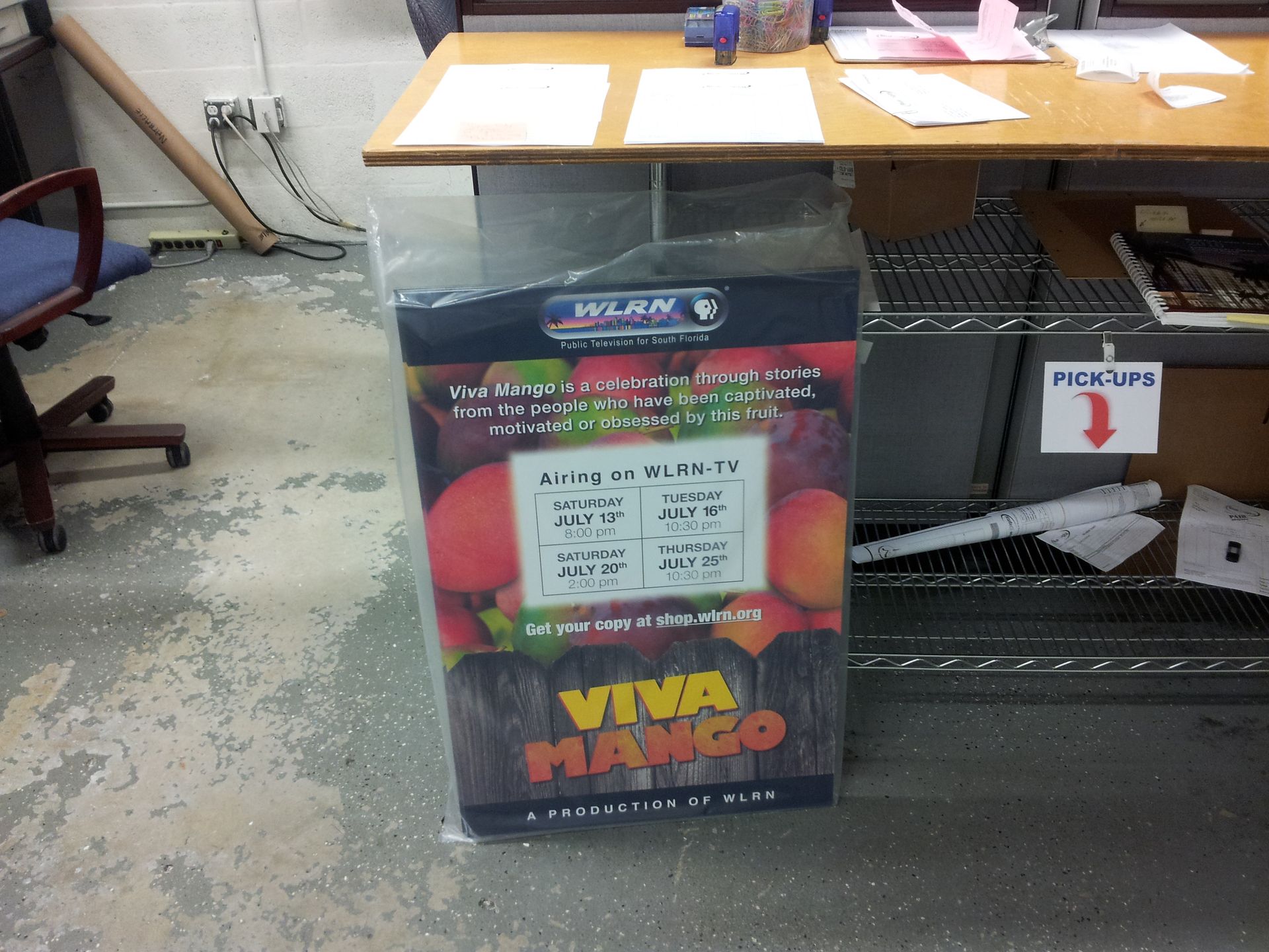 A Viva Mango promotional sign stands on the floor beneath a wooden desk in an office setting.