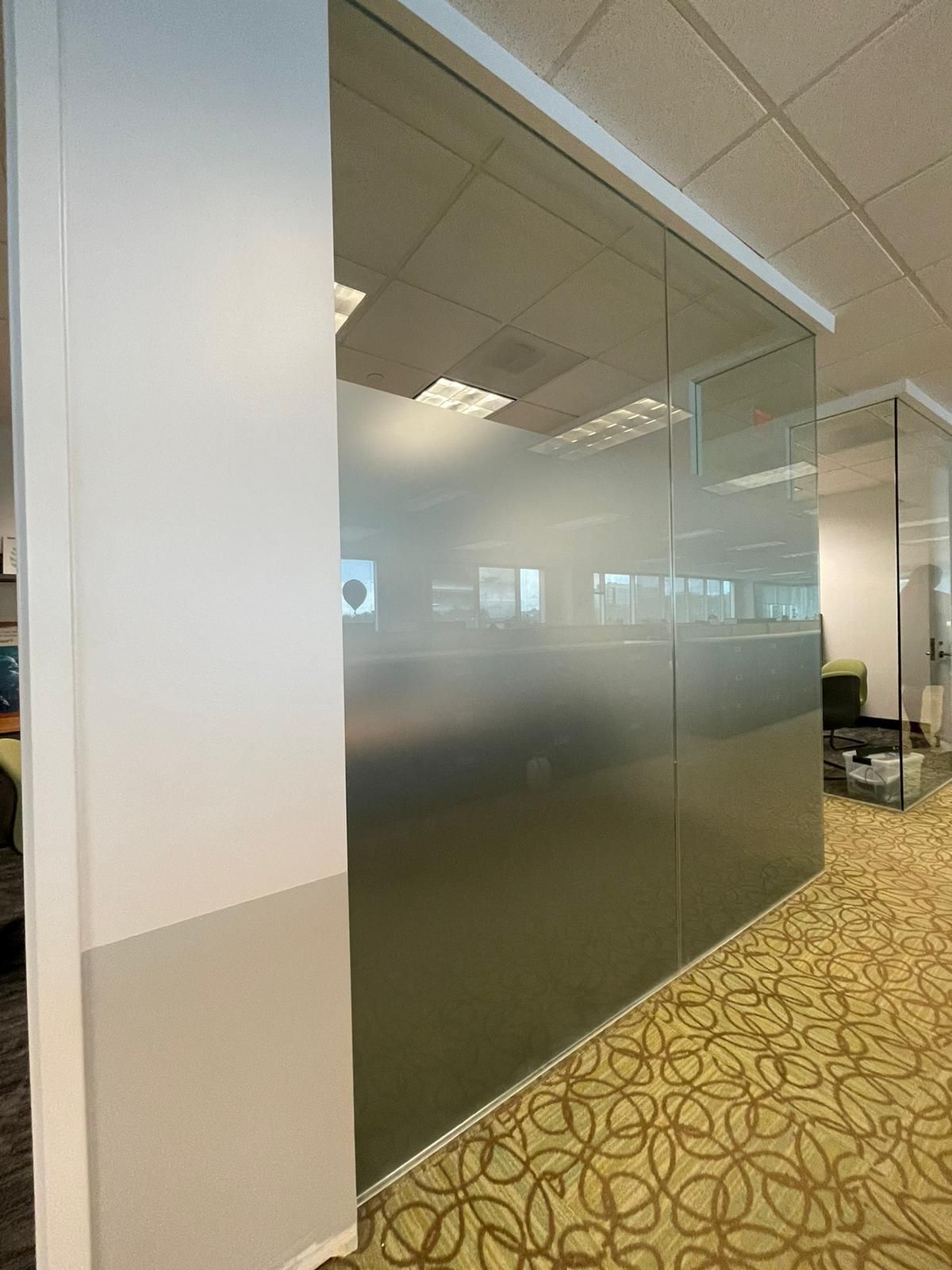 A wall with a frosted glass partition in an office setting featuring patterned carpet and ceiling tiles.