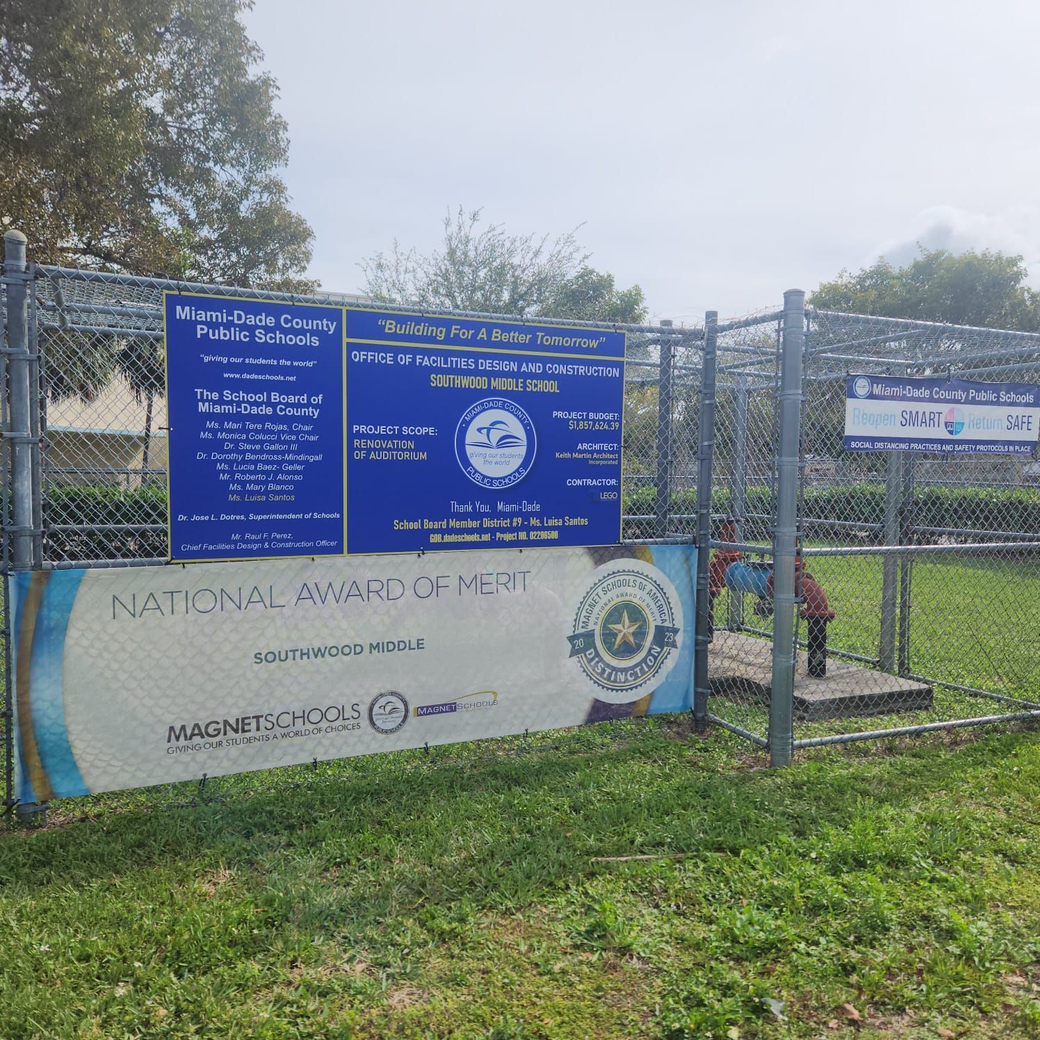 A chain-link fence displaying Miami-Dade County Public Schools signage and a National Award of Merit banner.